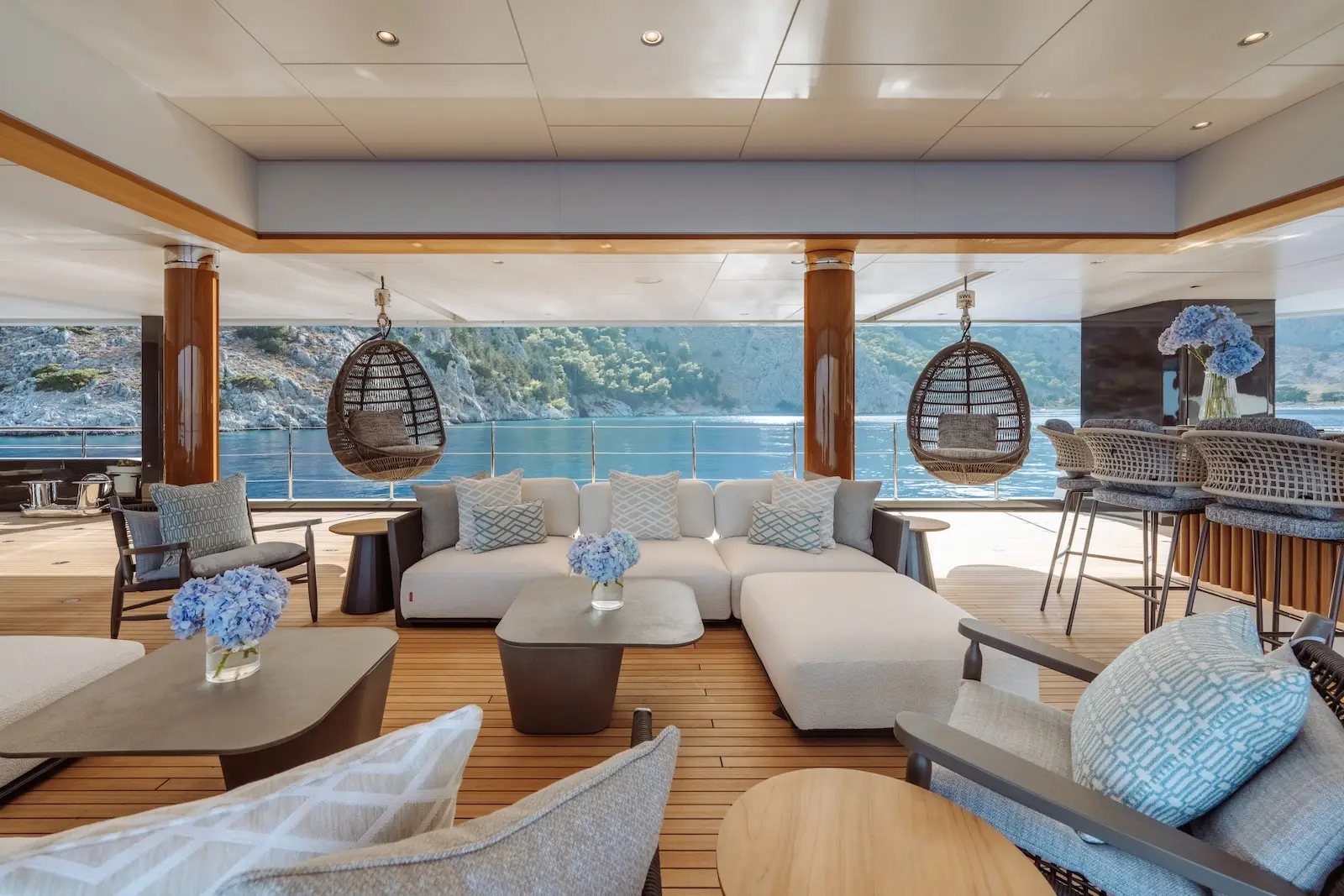 Shaded deck lounge with hanging chairs, teak decking and open sightlines to the water